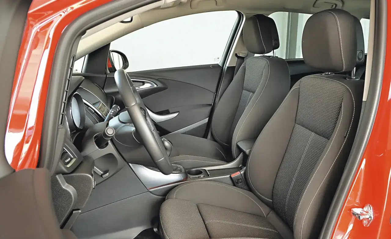 Wnętrze pomarańczowego Opla Astry J hatchback. Widok na przednie fotele, kierownicę i deskę rozdzielczą.