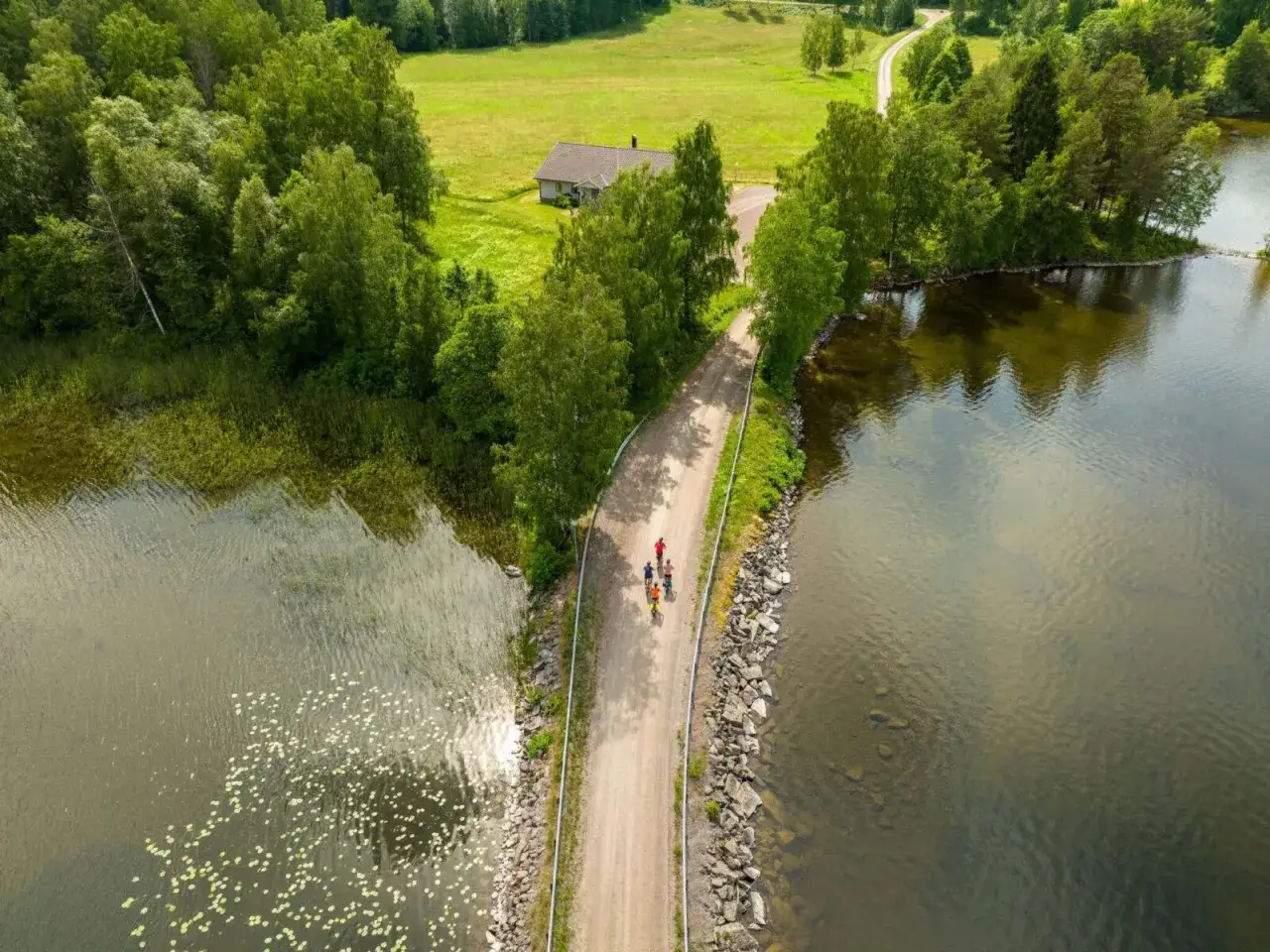 Familj cyklar l&auml;ngs en grusv&auml;g vid en sj&ouml;, en idyllisk vy &ouml;ver cykelleder Sverige.