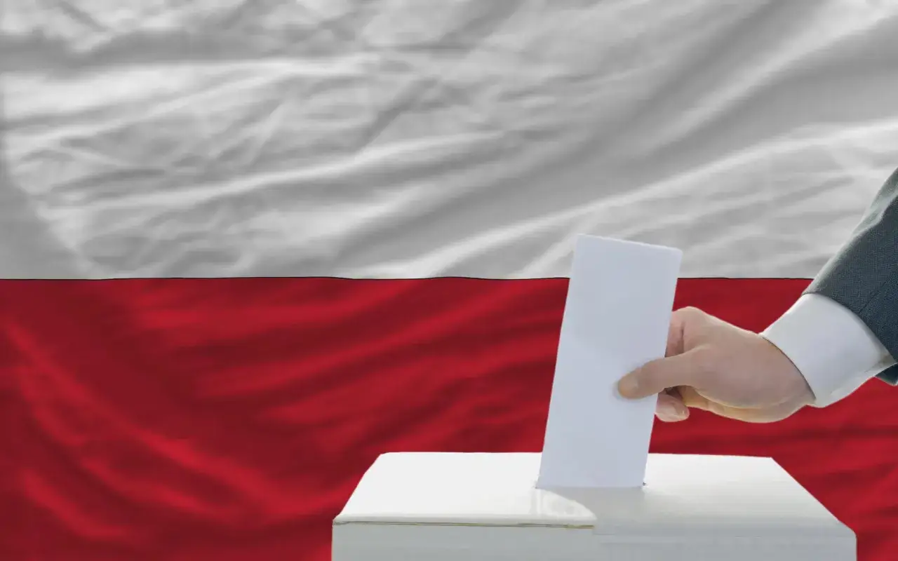 Dłoń wrzuca kartę do urny wyborczej na tle polskiej flagi. To symbol, kiedy referendum jest ważne.