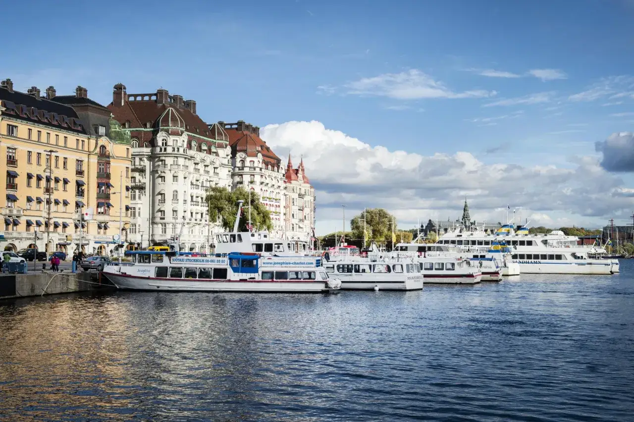 En båttur i Stockholm bjuder på vackra vyer av stadens arkitektur och vatten. Flera fartyg ligger förtöjda vid kajen.