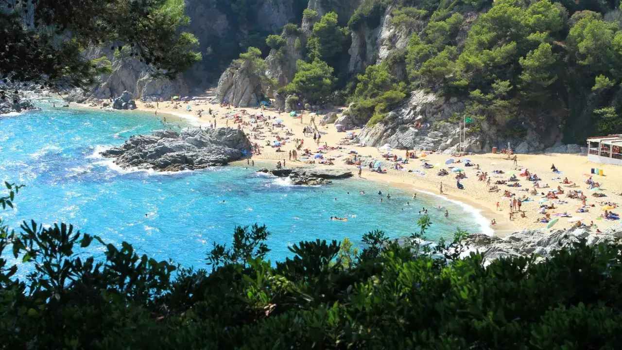 Una cala idílica con aguas turquesas y arena dorada, llena de gente disfrutando del sol. ¿Será esta la mejor playa de España?