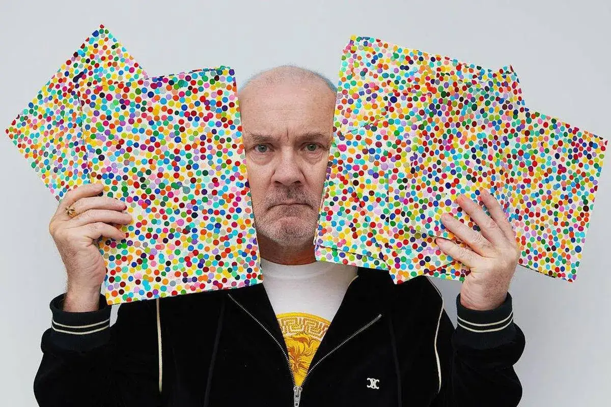 Damien Hirst holds up colorful dot paintings from his 