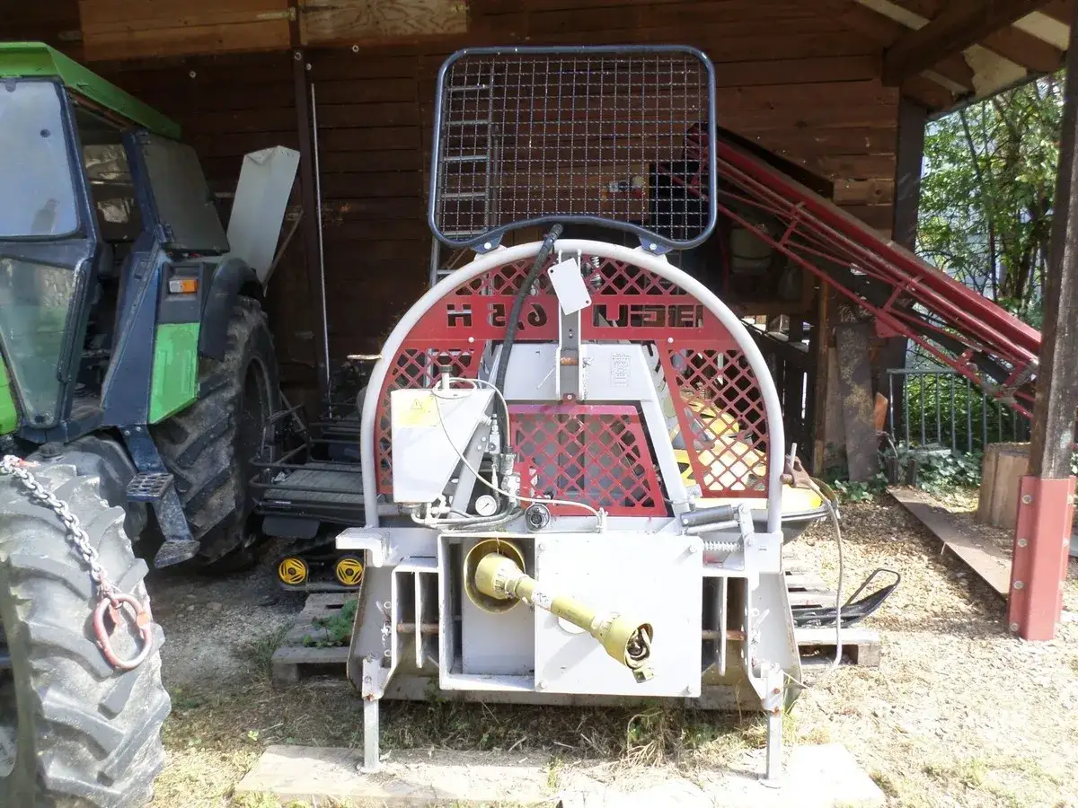 Eine BGU Seilwinde mit Traktor im Hintergrund. Die Winde hat ein rotes Gitter und ist für den Forstwirtschaftseinsatz konzipiert.