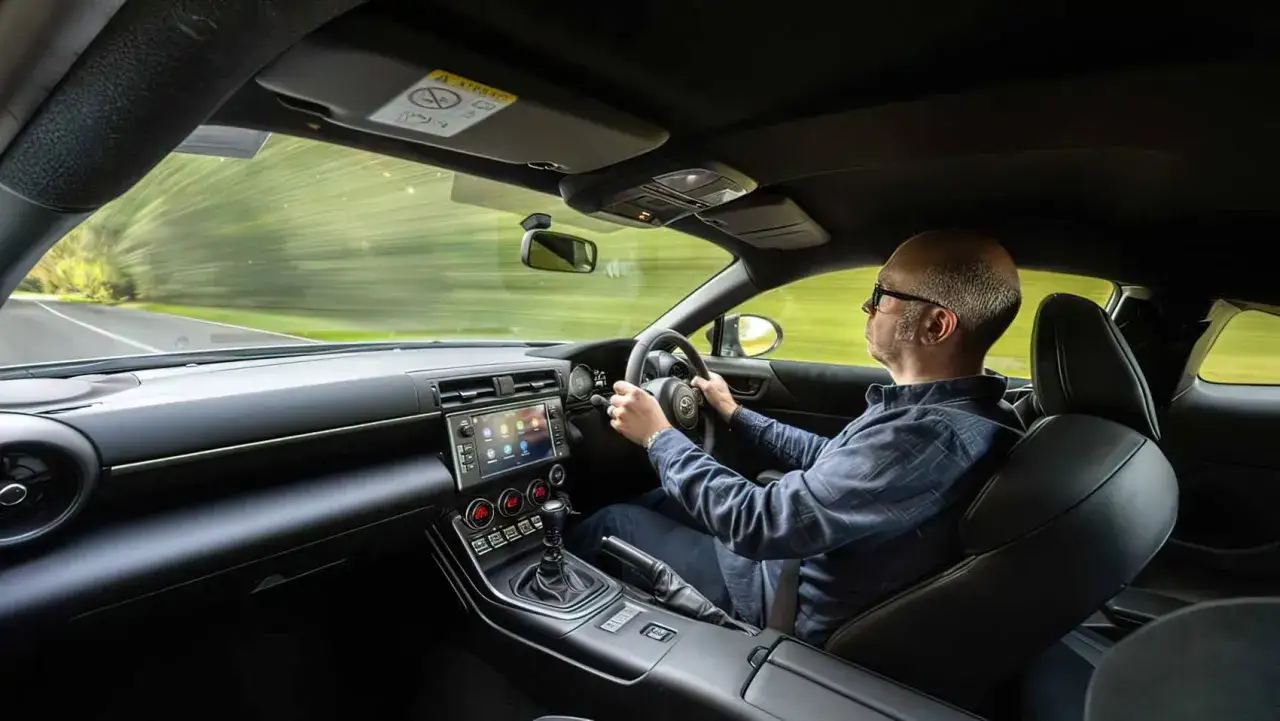 Mężczyzna za kierownicą Toyoty 86, cieszący się jazdą po malowniczej drodze.