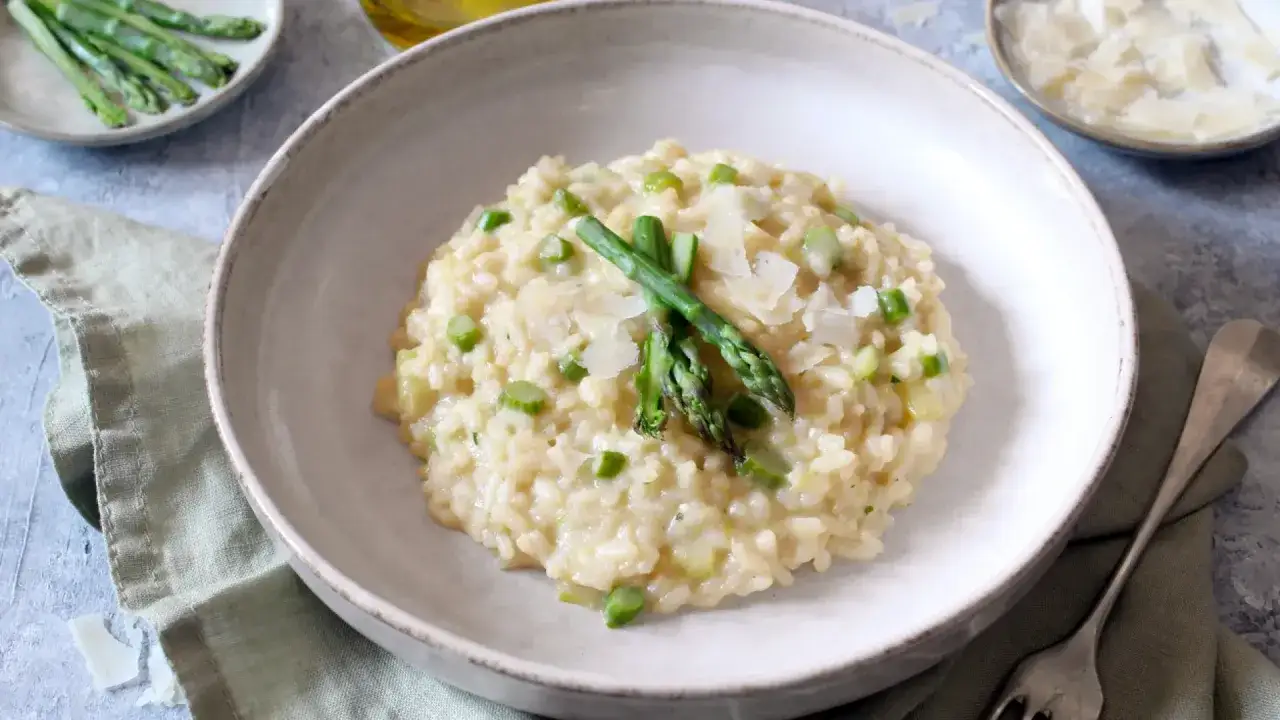 Cremoso risotto de esparragos, adornado con espárragos frescos y lascas de queso parmesano. Un plato perfecto para disfrutar de la primavera.