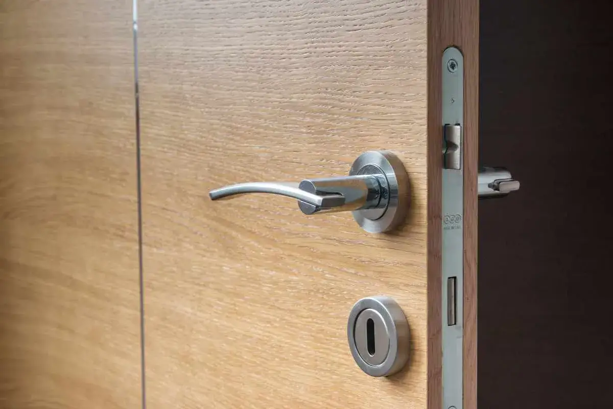 Maniglia e serratura di una porta in legno chiaro, con la porta socchiusa. Si sente il cigolio della porta.
