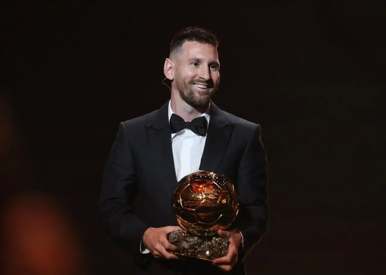 Uśmiechnięty Lionel Messi na gali Złotej Piłki, trzymający w dłoniach prestiżową statuetkę.