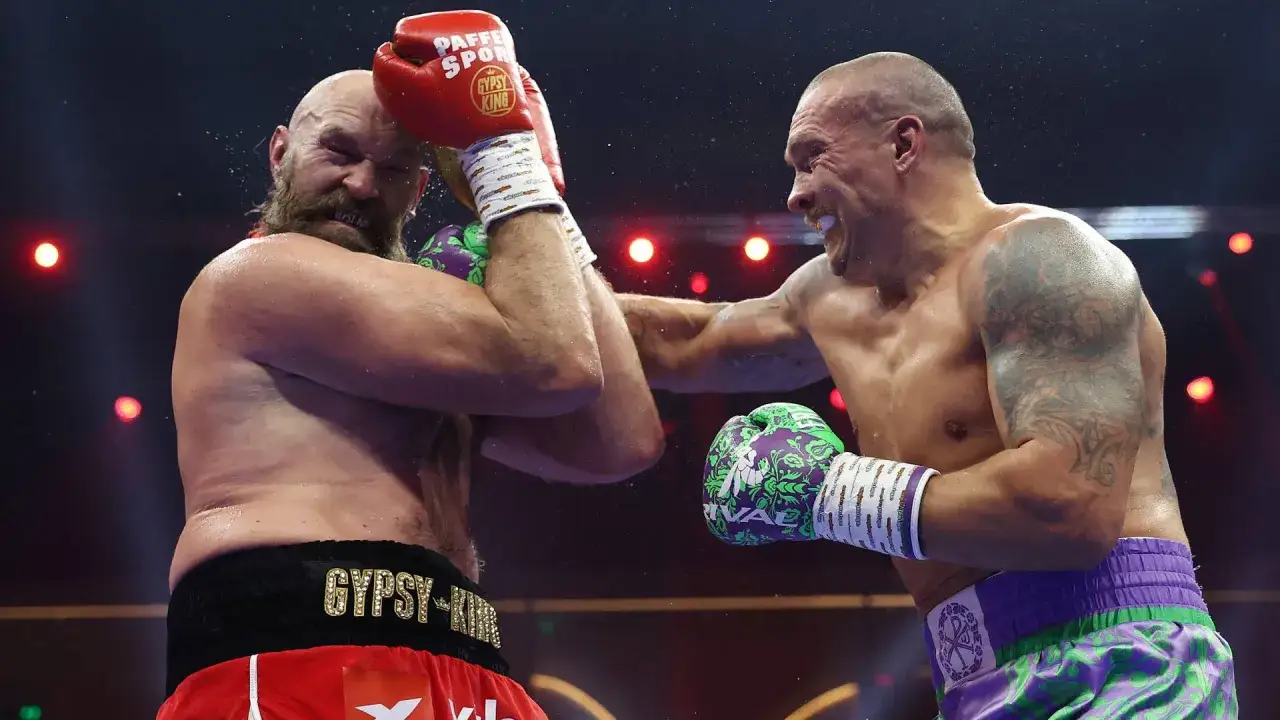 Two boxers, one with a beard and red shorts, the other with tattoos and purple shorts, clash in a cruiser weight bout.