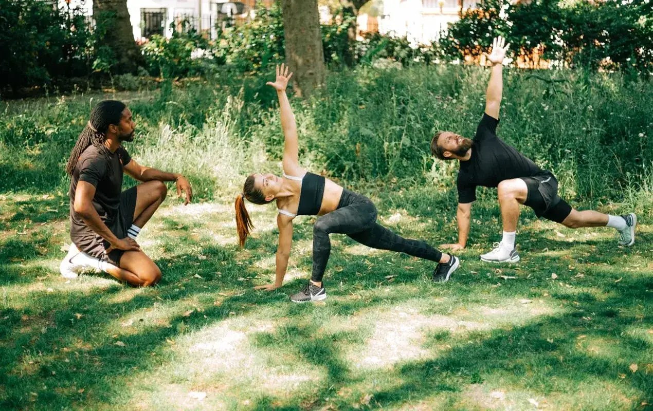 Un coach observe deux participants en plein exercice de yoga lors d'un bootcamp sport en extérieur.