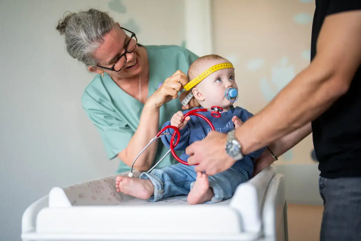 Sjuksköterska mäter ett års vaccin-barns huvudomfång. Pappa håller barnet.