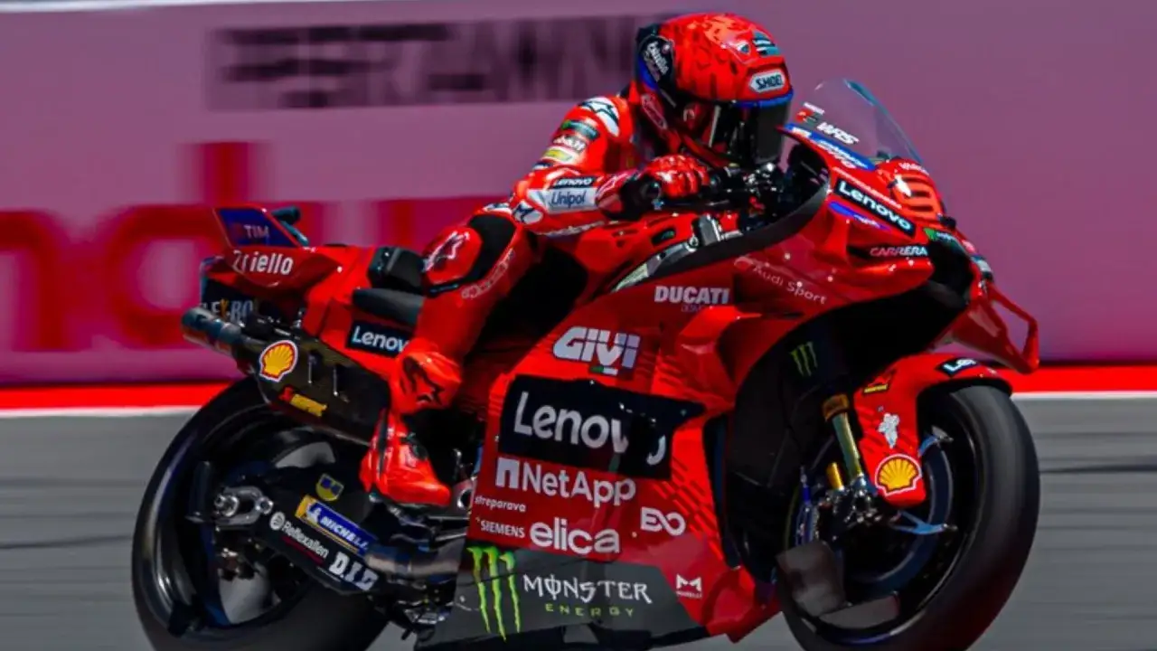 Piloto de Ducati en carrera, con su traje rojo y casco. La moto luce patrocinadores como Lenovo y Monster Energy. A pesar de su edad, la pasión por la velocidad es evidente en su pilotaje.