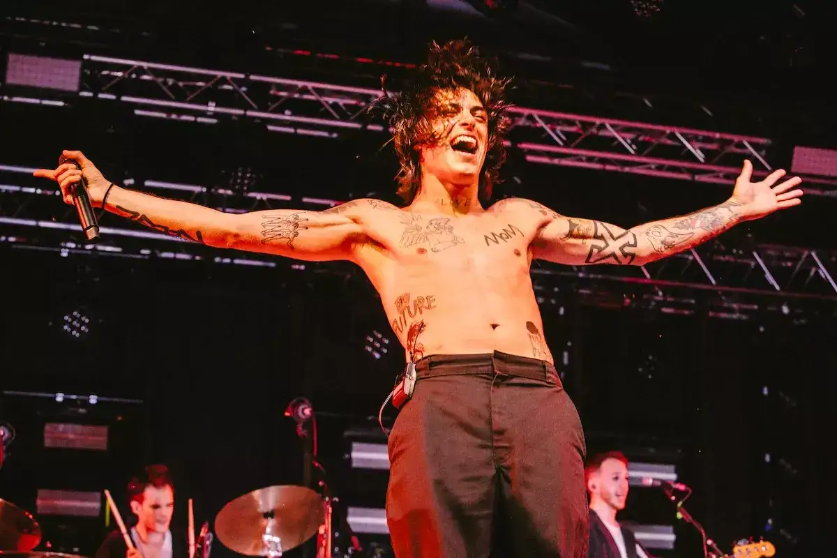 Micky Paiano sul palco, a torso nudo e con tatuaggi, canta con passione, braccia aperte, microfono in mano.