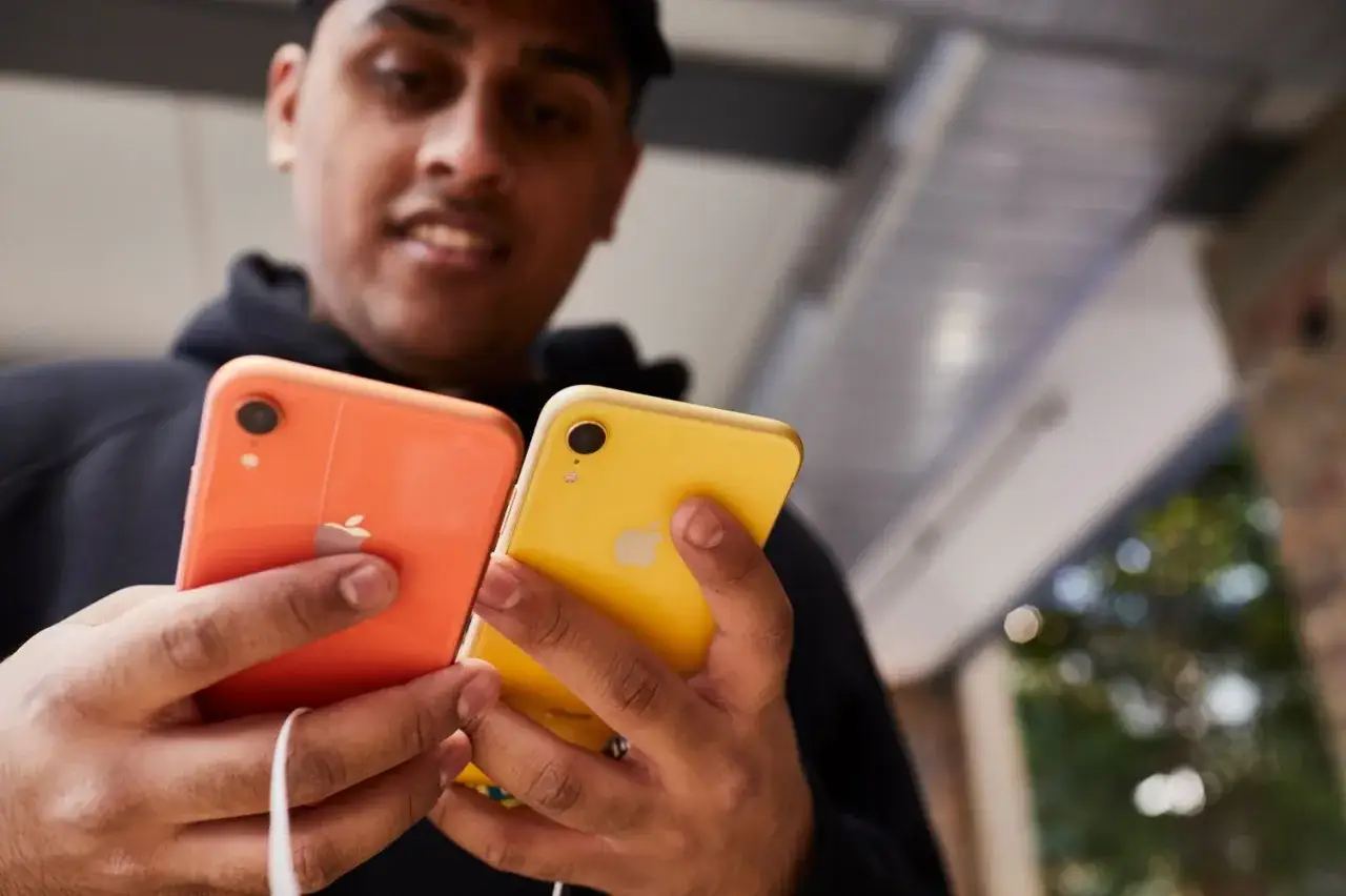 Mężczyzna trzyma dwa telefony: pomarańczowy i **iphone xr żółty**.