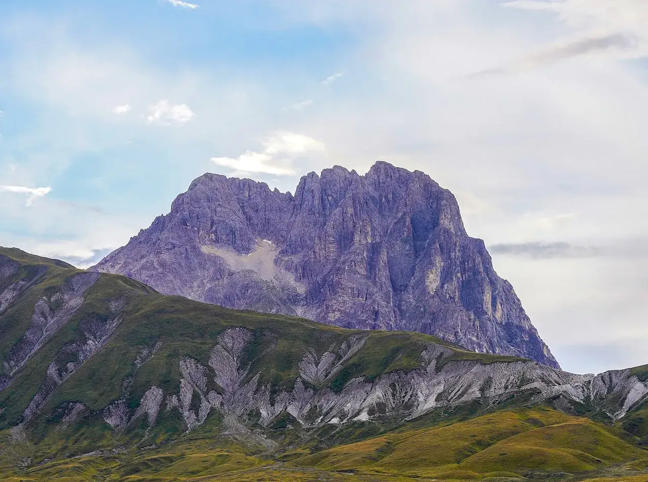 Vasto campo imperatore ai piedi del Gran Sasso, con dolci colline verdi e un maestoso massiccio roccioso sullo sfondo.