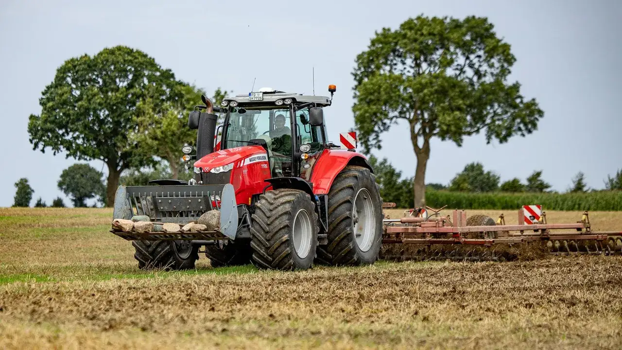 Roter Traktor mit Steinegreifer und Grubber im Feld. Die Kfz-Steuer für diesen Traktor ist sicher gut investiert.