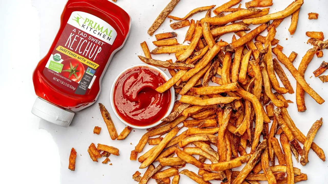Montón de patatas fritas crujientes junto a un cuenco de kétchup y una botella de Primal Kitchen.