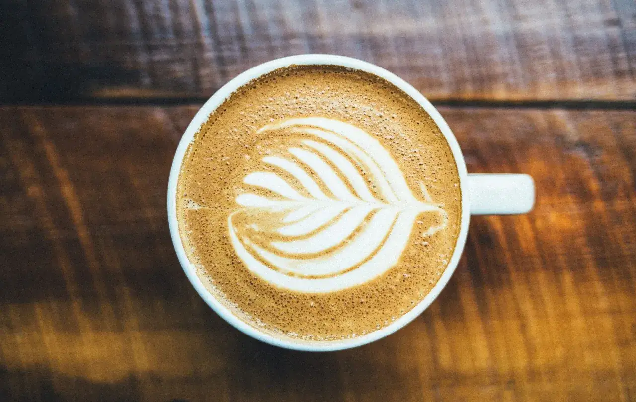 Un cappuccino con latte art su un tavolo di legno. Chiss&agrave; chi ha inventato il cappuccino?