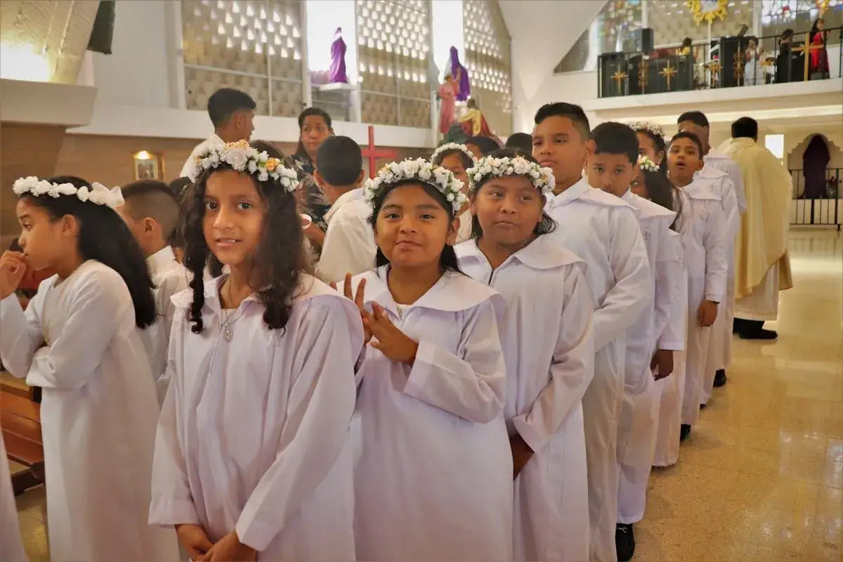Des enfants en robe blanche et couronnes de fleurs attendent leur bapt&ecirc;me chr&eacute;tien dans une &eacute;glise.