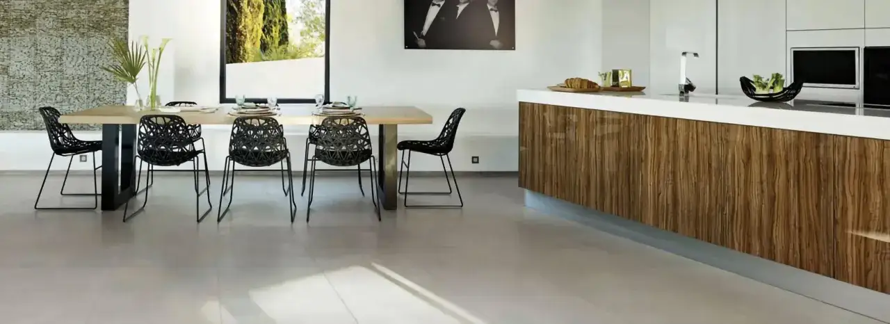 Un salon moderne avec une table en bois, des chaises noires design et un sol en revêtement carrelage clair. L'îlot de cuisine en bois veiné complète l'ensemble.