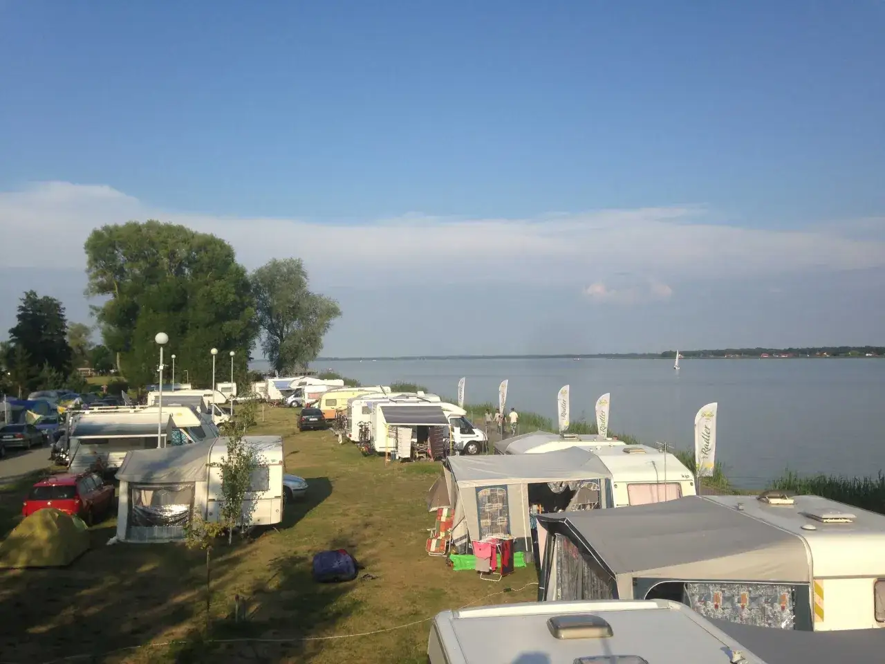 Wiele przyczep kempingowych i namiotów rozbitych nad jeziorem. To idealne miejsce na camping na granicy, gdzie można podziwiać wodę i żaglówki.