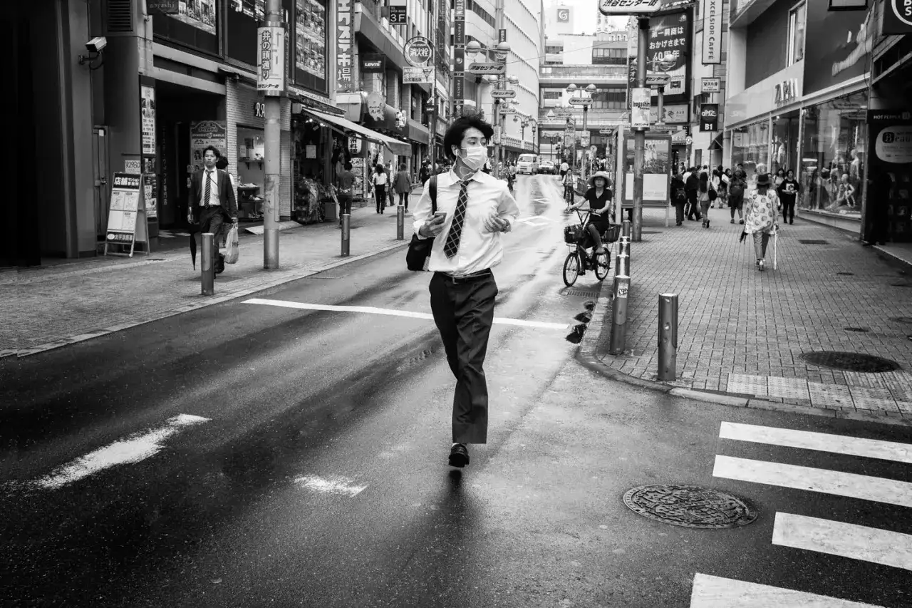 Mężczyzna w masce biegnie przez mokrą ulicę w Tokio, uchwycony w klasycznym stylu leica street photo.