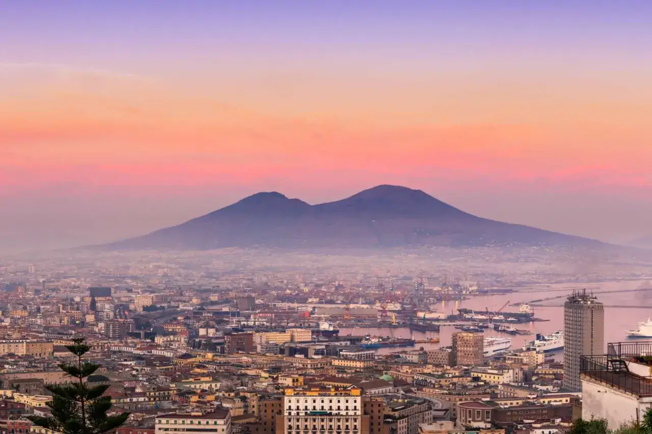 The city of Naples, Italy, is nice, with Mount Vesuvius looming in the background under a pastel sky.