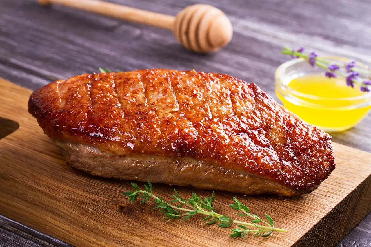 Un magret de canard au barbecue, la peau dorée et croustillante, prêt à être dégusté avec une touche de miel et de thym.