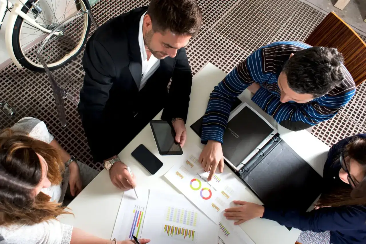 Un coach de negocios gu&iacute;a a un equipo en una reuni&oacute;n, analizando gr&aacute;ficos y datos en una mesa de trabajo.