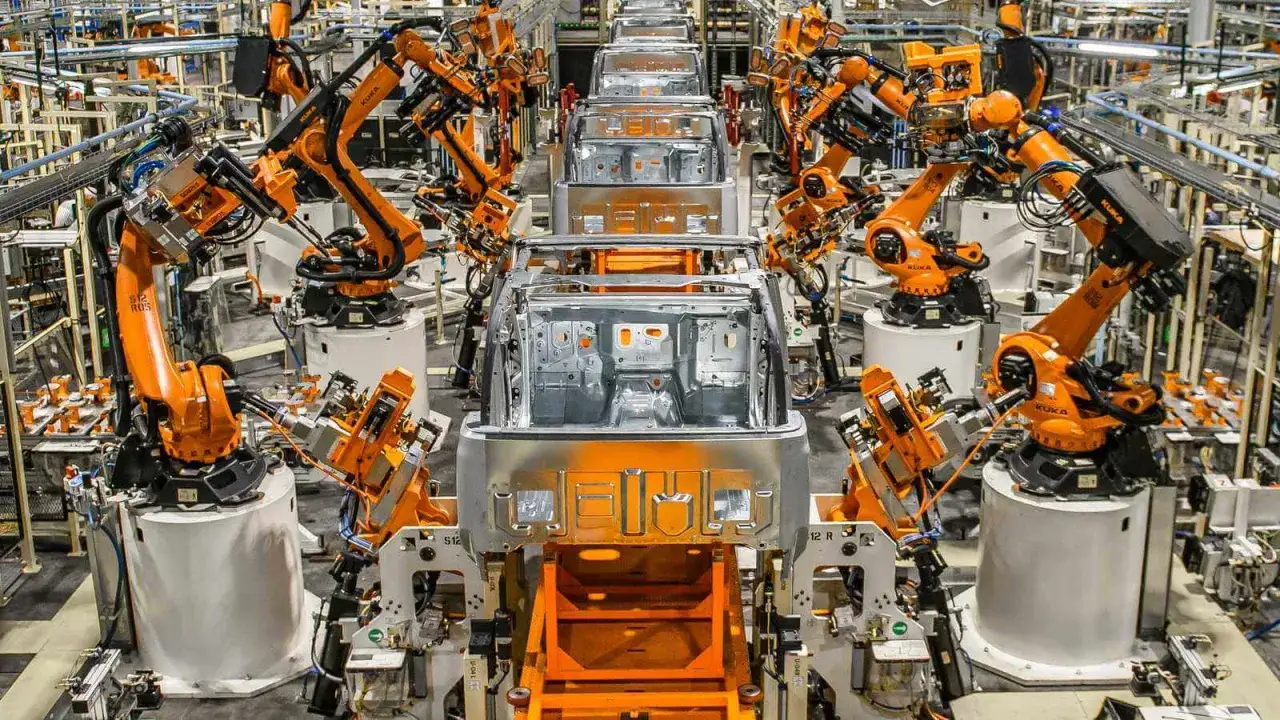 Bracci robotici arancioni lavorano su telai di auto in una fabbrica. La meccatronica cos'è? È l'integrazione di meccanica, elettronica e informatica per creare sistemi automatizzati.