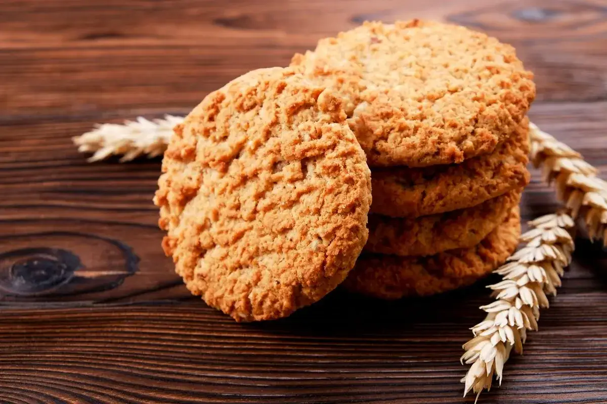 Biscotti integrali da colazione, dorati e croccanti, con spighe di grano su un tavolo di legno scuro.