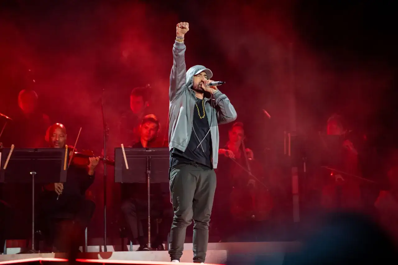 Kto to Eminem? Raper na scenie z podniesioną pięścią, w tle orkiestra smyczkowa.
