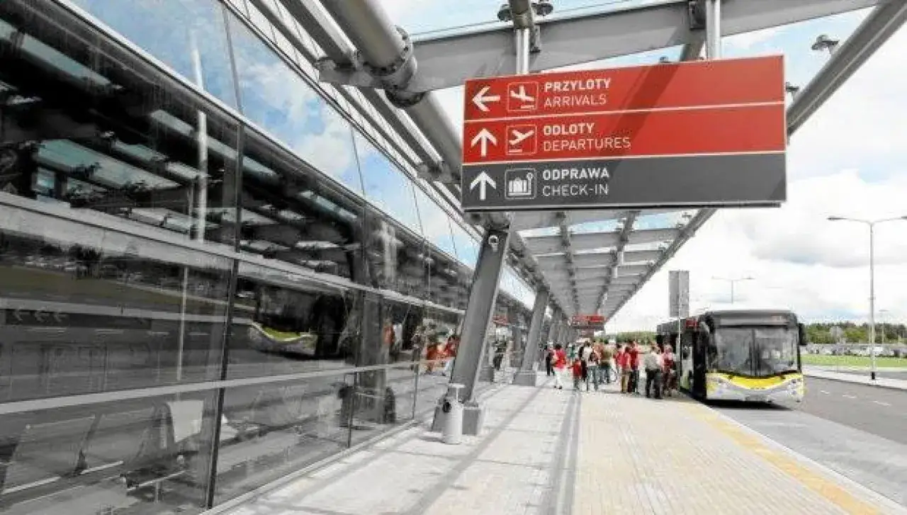 Przed odlotem z Modlina, pasażerowie wsiadają do autobusu. Tablice kierują do przylot&oacute;w, odlot&oacute;w i odprawy.