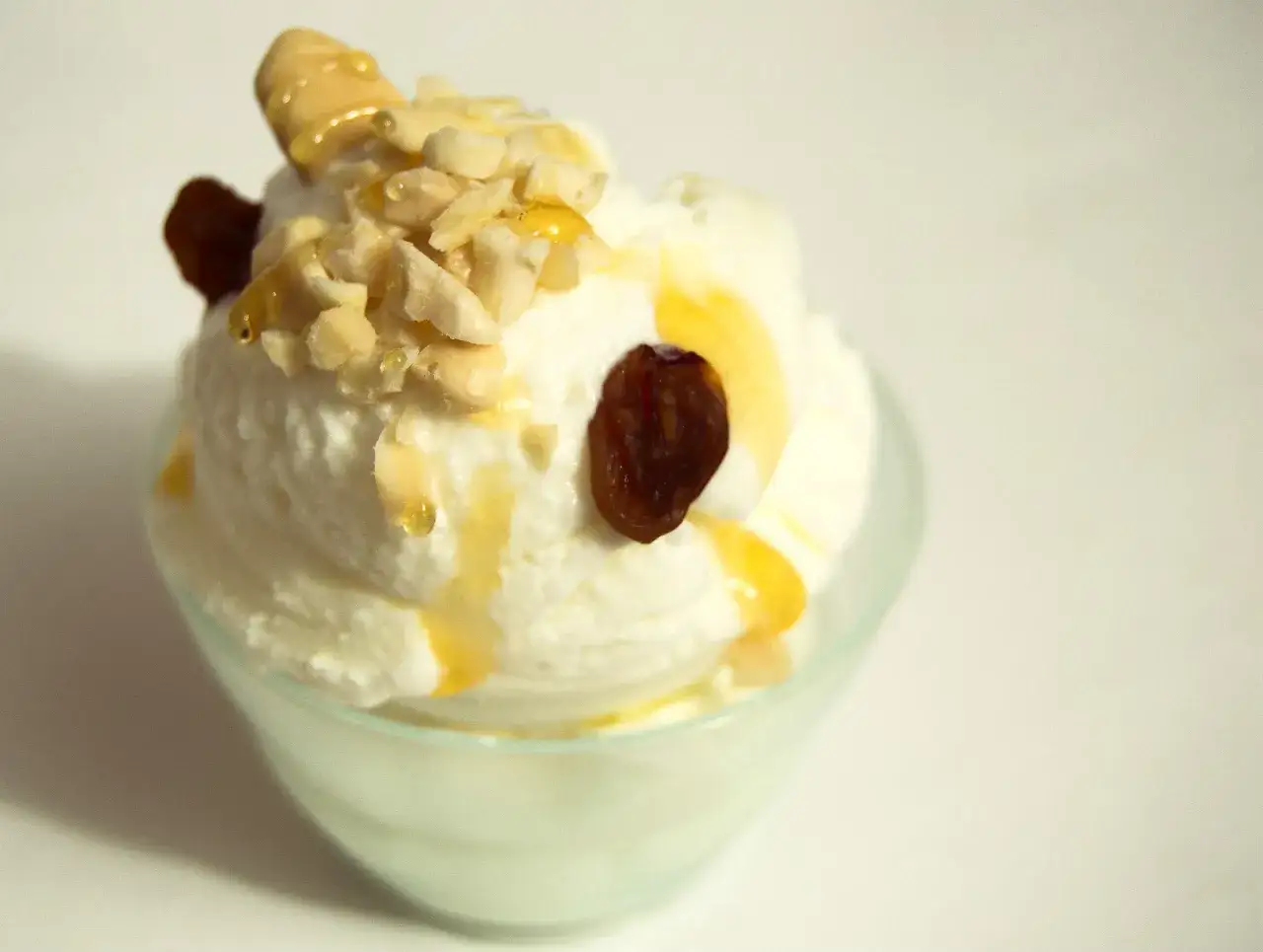 Delizioso gelato con yogurt greco, guarnito con mandorle tritate, uvetta e un filo di miele dorato.