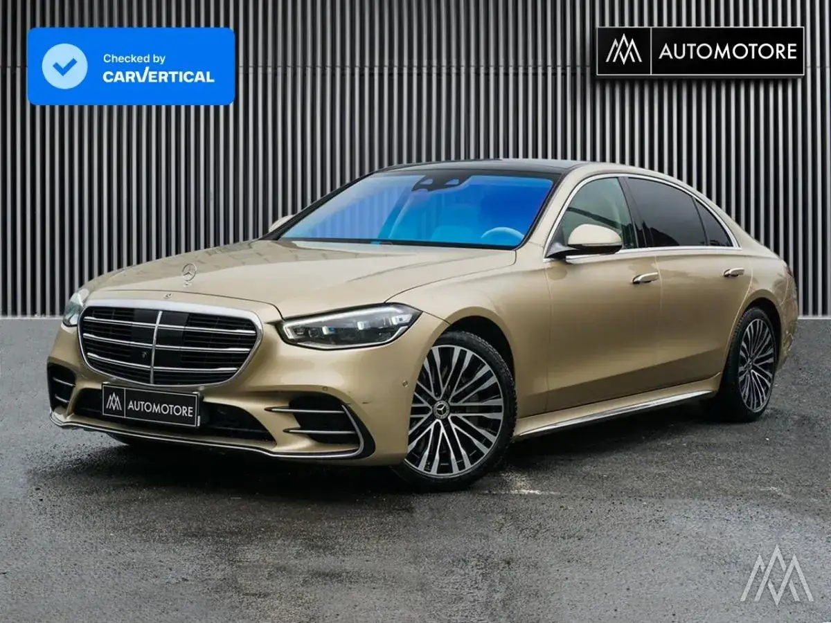 Elegancki, złoty Mercedes S400d prezentuje się imponująco na tle nowoczesnej fasady.