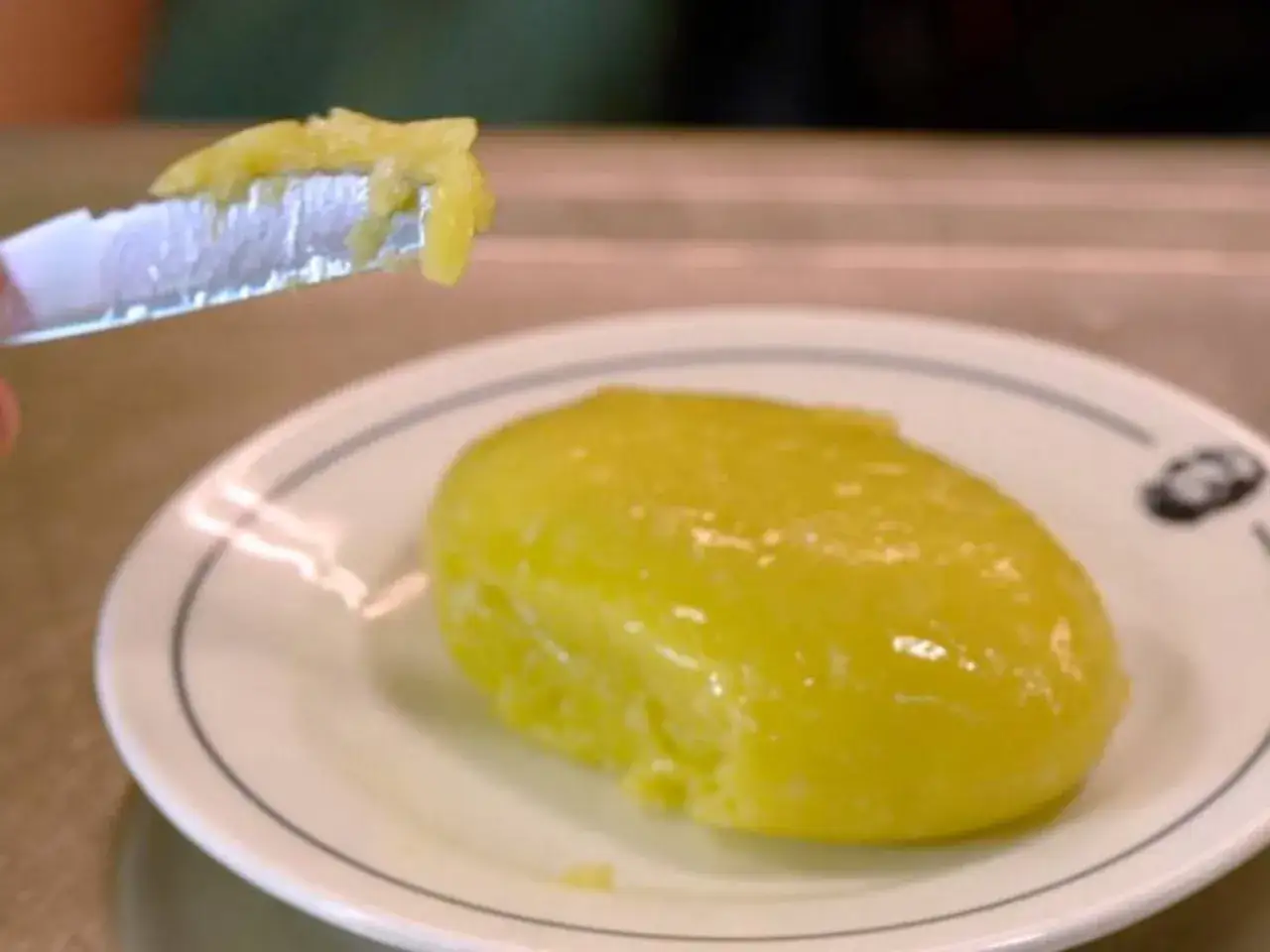 Un trozo de alioli con leche sobre un plato blanco. Un cuchillo con un poco de alioli en la punta.