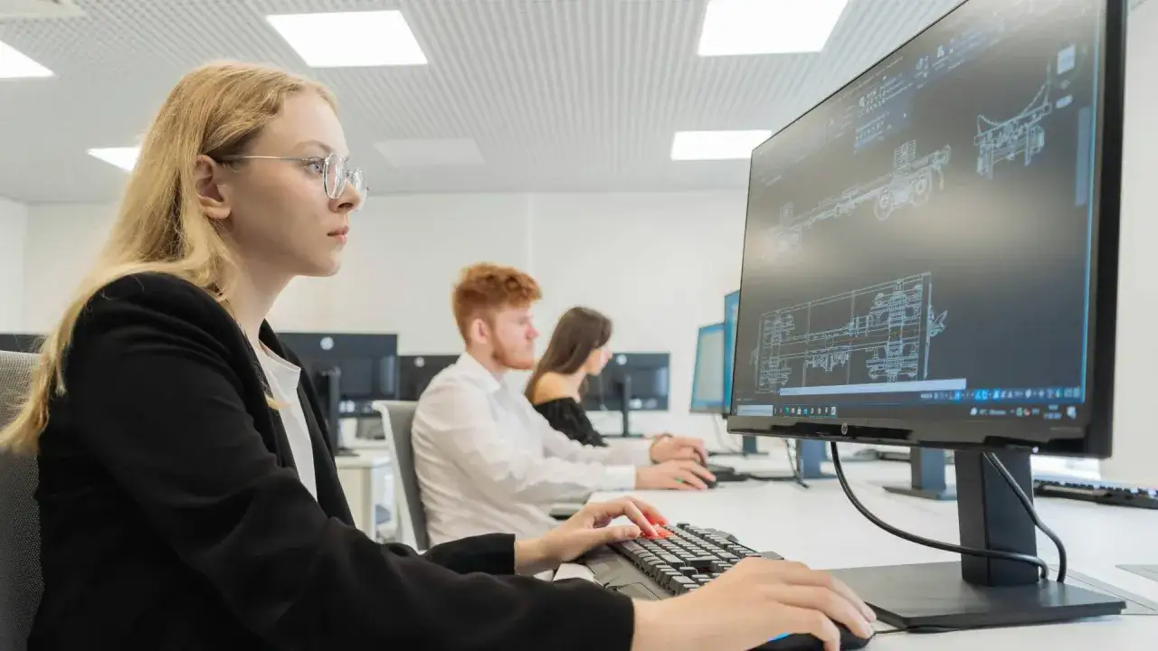 Studentka podczas praktyk na studiach pracuje przy komputerze, projektując skomplikowane detale techniczne.