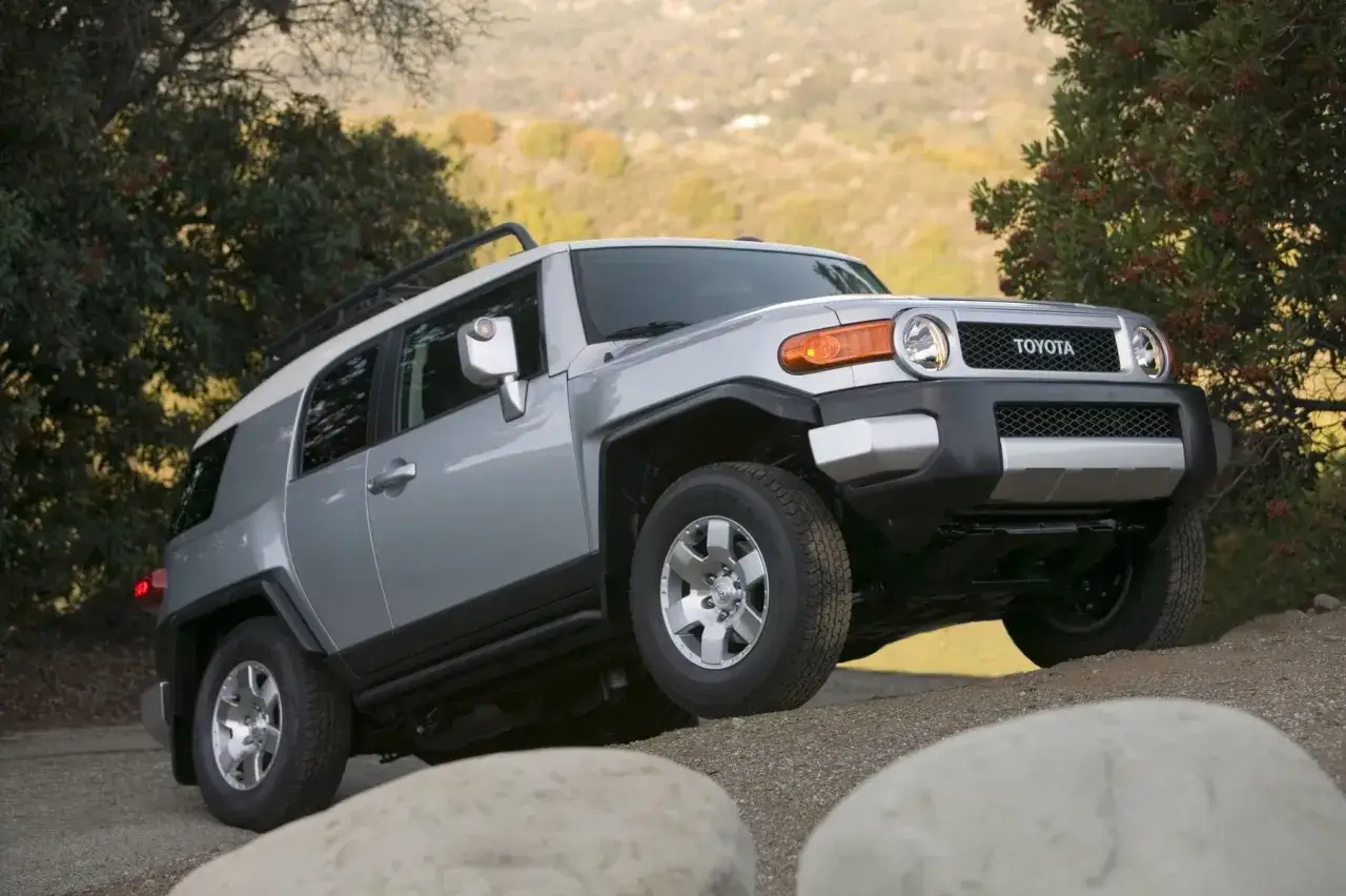 Srebrny Toyota FJ Cruiser pokonuje nierówny teren, gotowy na przygodę.