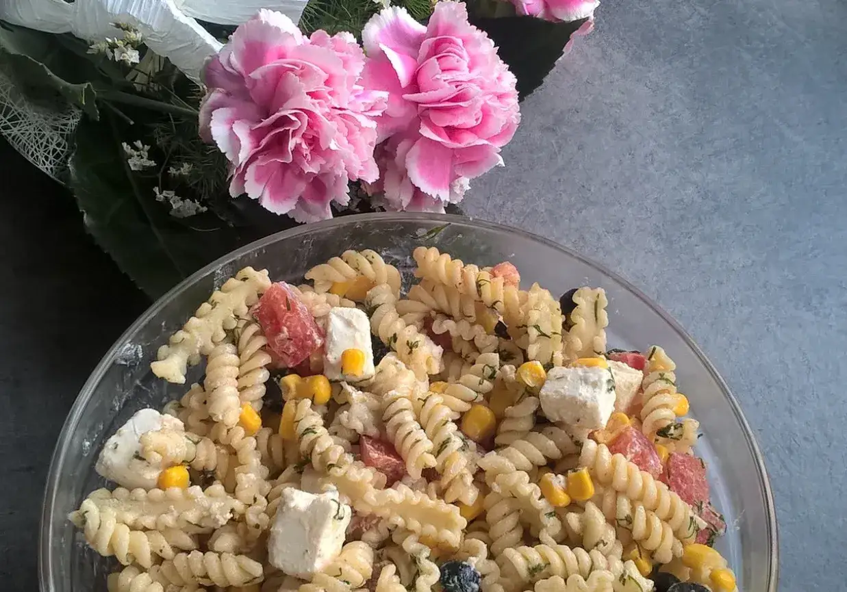 Pyszna sałatka z makaronem fusilli z fetą, pomidorkami i kukurydzą, ozdobiona różowymi kwiatami.