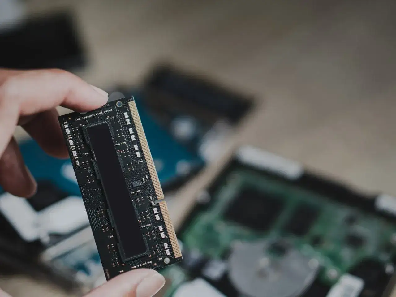 Dłoń trzyma moduł pamięci RAM, prawdopodobnie LPDDR5, z widocznymi układami scalonymi. W tle widać inne komponenty komputerowe.