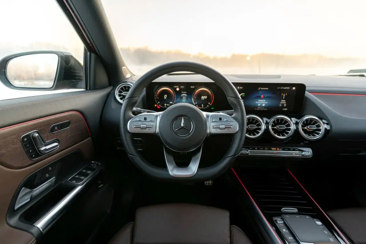 Wnętrze Mercedesa GLA 220 z nowoczesnym kokpitem, cyfrowymi zegarami i ekranem multimedialnym. Skórzana tapicerka i drewniane wstawki dodają elegancji.