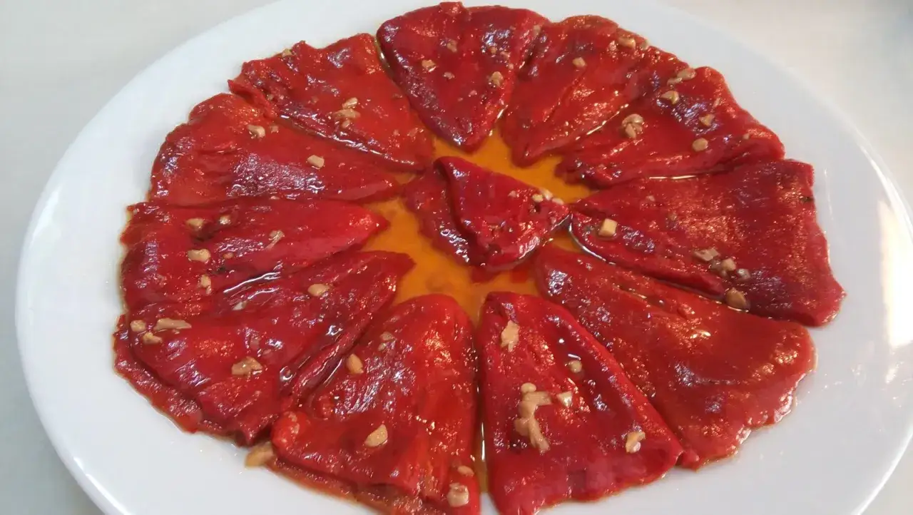 Pimientos del piquillo asados, cortados en tiras y ali&ntilde;ados con aceite y ajo, servidos en un plato blanco.