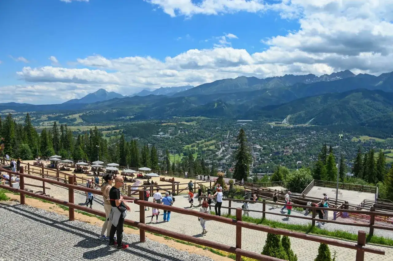 Widok z Gubał&oacute;wki na Tatry i Zakopane. Tłumy turyst&oacute;w podziwiają panoramę, korzystając z licznych atrakcji.