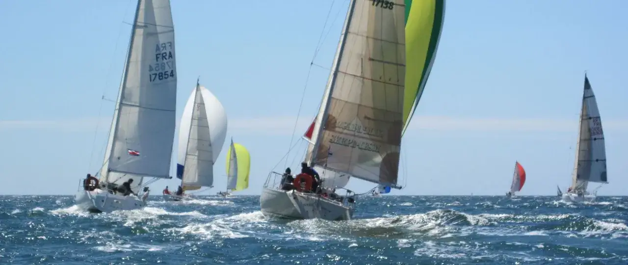 Course de voiliers par temps clair. Un voilier avec une voile verte et beige, nommé 