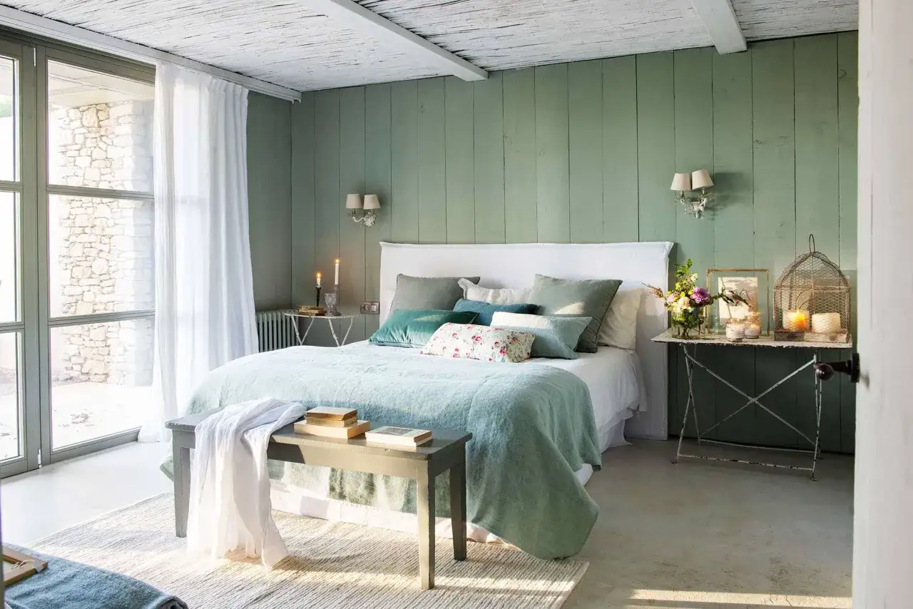Acogedor dormitorio verde agua y blanco con cama mullida, cojines y luz natural.