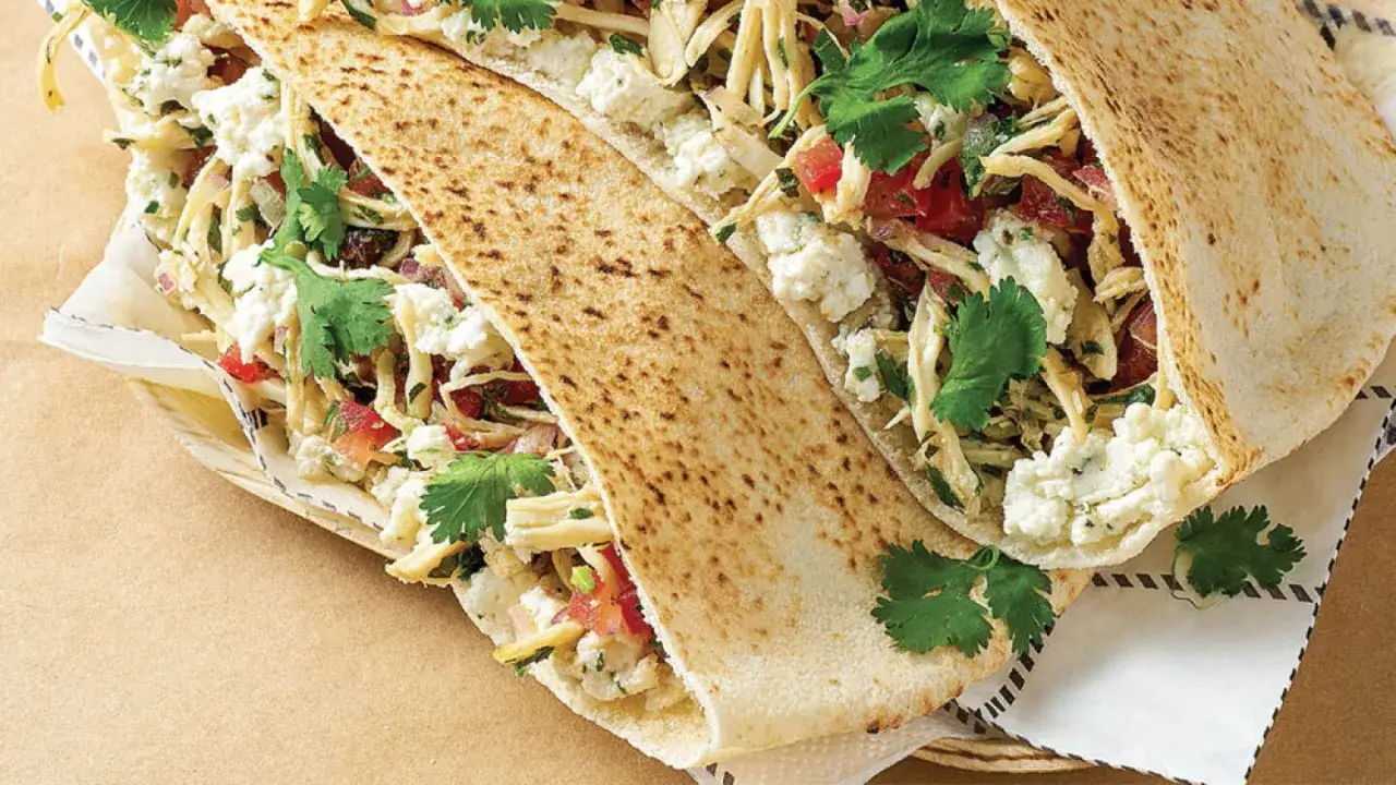 Dos panes de pita rellenos de pollo deshebrado, queso fresco desmoronado, tomate picado y cilantro fresco.