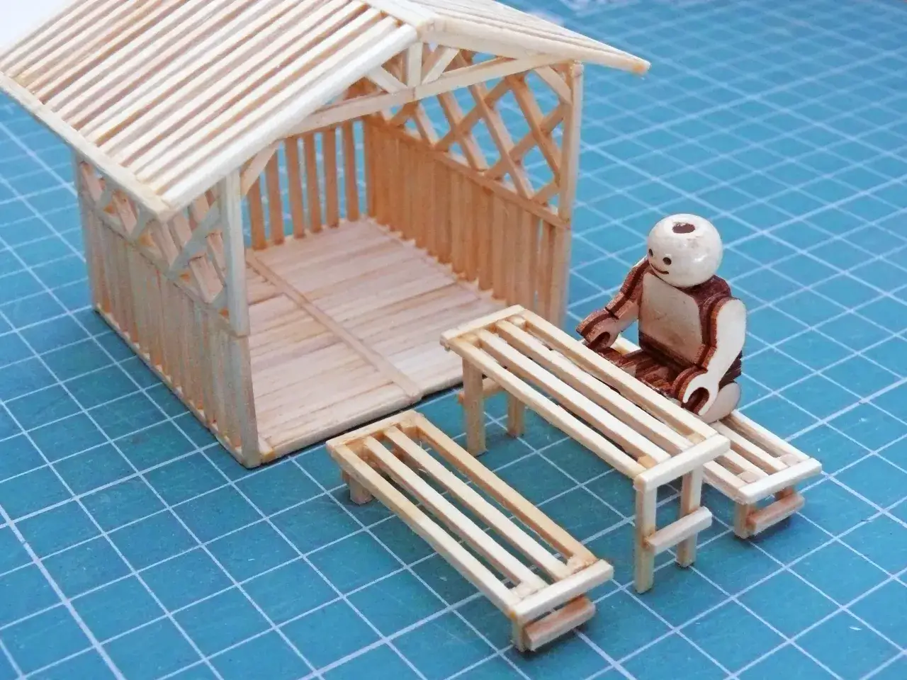 Miniaturowy domek z zapałek, z ławkami i ludzikiem. Inspiracja, jak zrobić domek z zapałek.