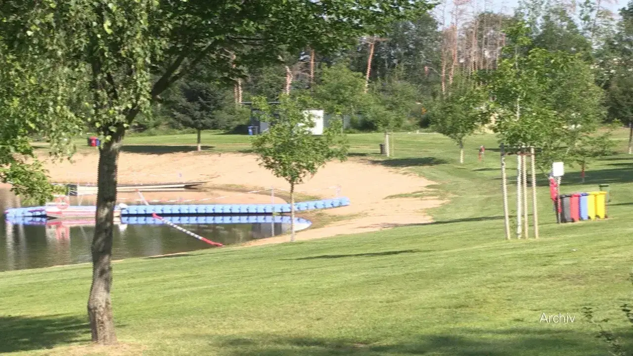 Ein sonniger Tag am Erlabrunner Badesee. Ein Steg aus blauen Pontons f&uuml;hrt ins Wasser, daneben ein Sandstrand und gr&uuml;ne Liegewiesen.