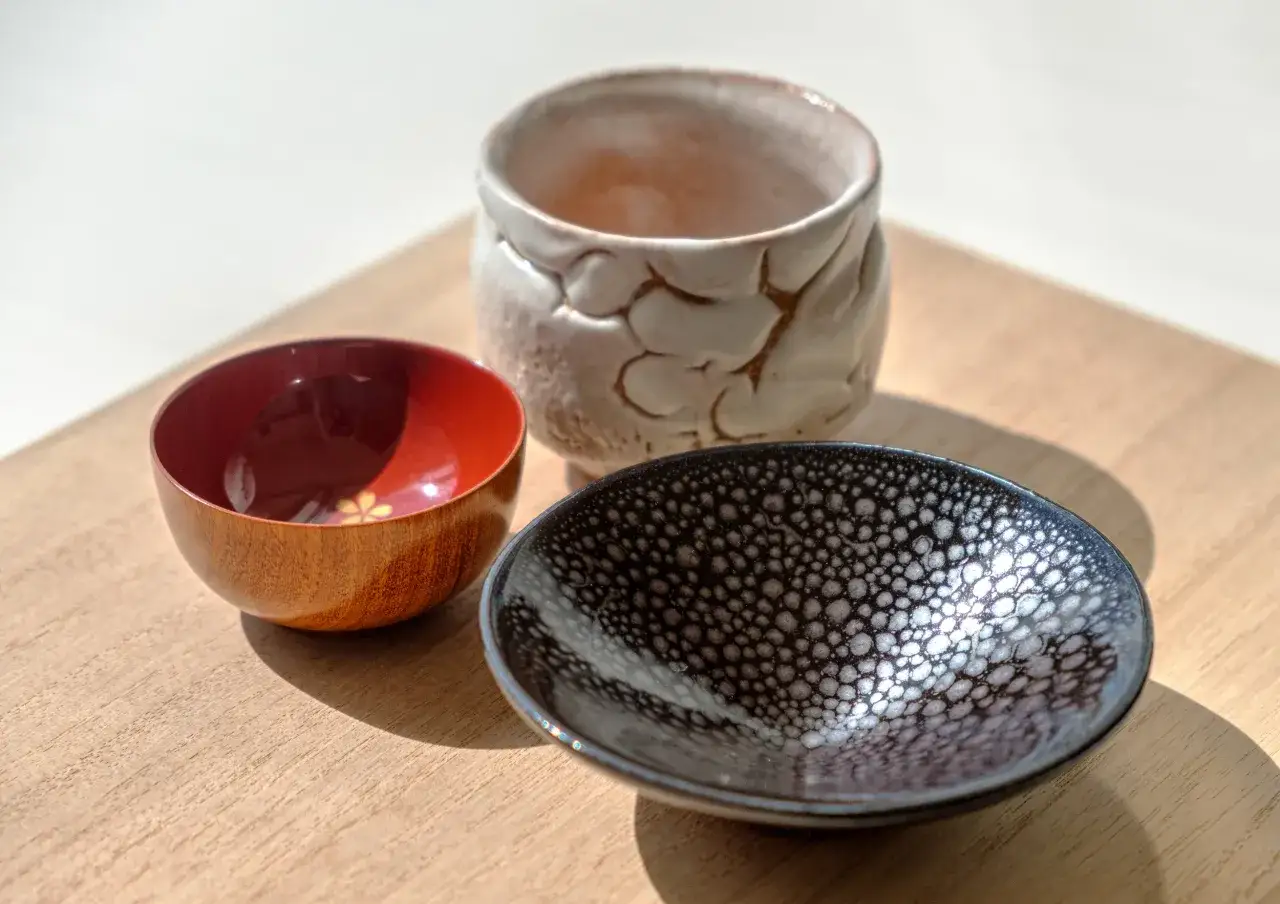 Trzy naczynia do sake: drewniana miseczka z czerwonym wnętrzem, czarna z białymi kropkami i ceramiczny kubek. Zastanawiasz się, sake ile procent?