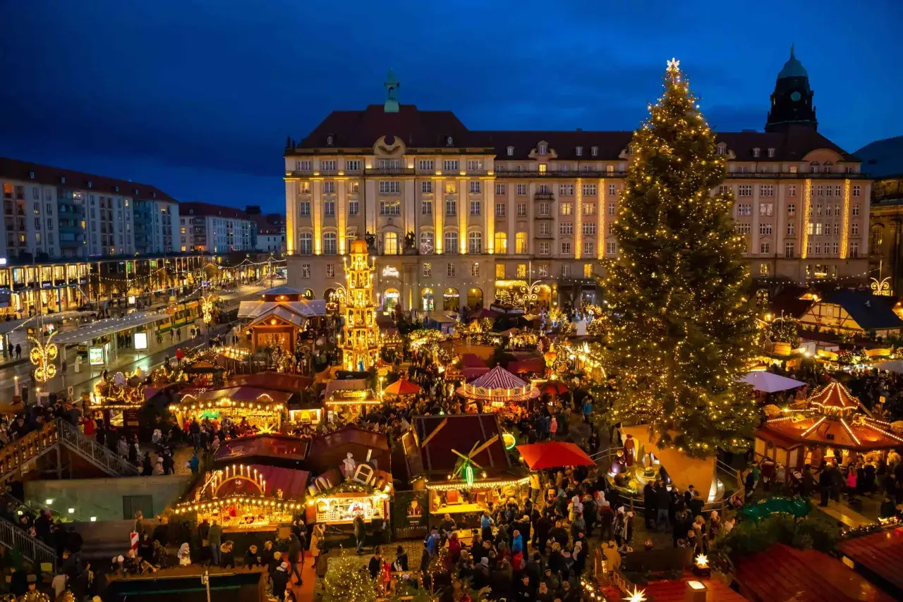 Tłoczny jarmark w Dreźnie nocą, rozświetlony tysiącami lampek. W centrum ogromna choinka, obok tradycyjna piramida bożonarodzeniowa.