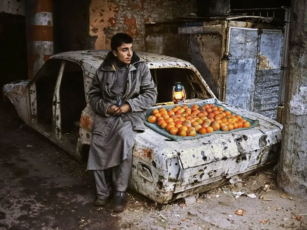 Un giovane vende arance su un'auto distrutta, un'opera d'arte di Steve McCurry. La scena è illuminata da una lanterna.